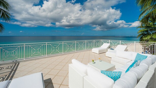 Eine Terrasse mit weißer Gartenmöbeln, Blick auf das Meer und einem dekorativen Geländer.