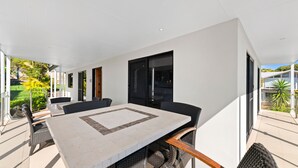 Uma área moderna para refeições ao ar livre, com uma mesa grande e cadeiras, cercada por paredes e portas de vidro.