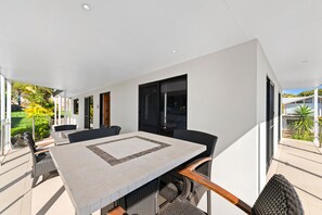 Een moderne eethoek buiten met een grote tafel en stoelen, omringd door glazen wanden en deuren.