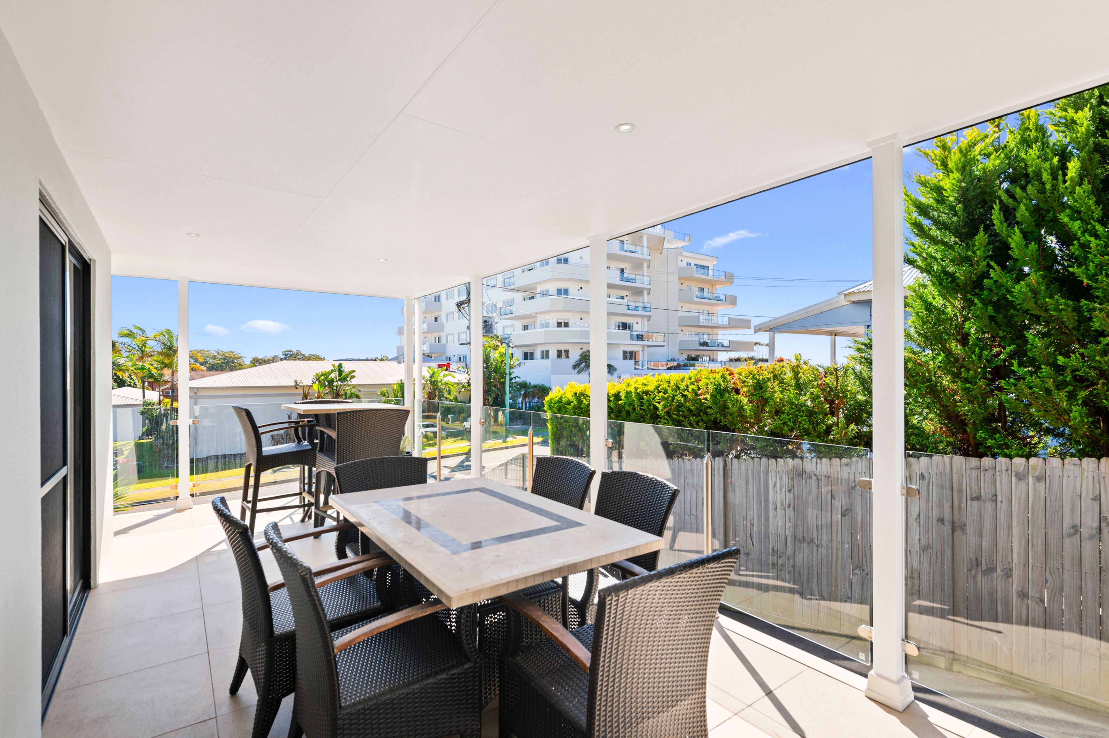 A balcony with a table and chairs, large windows, and a view of a residential area.