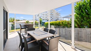 Un balcón con mesa y sillas, ventanas amplias y vista a una zona residencial.