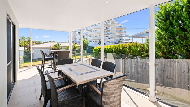Varanda com mesa e cadeiras, janelas amplas e vista para uma área residencial.