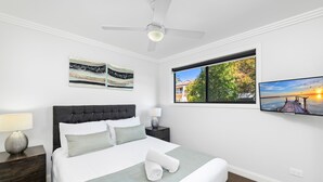 Quarto com cama, mesa de cabeceira, luminária, ventilador de teto e obras de arte nas paredes.