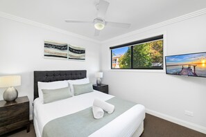 Een slaapkamer met een bed, nachtkastje, lamp, plafondventilator en kunst aan de muur.