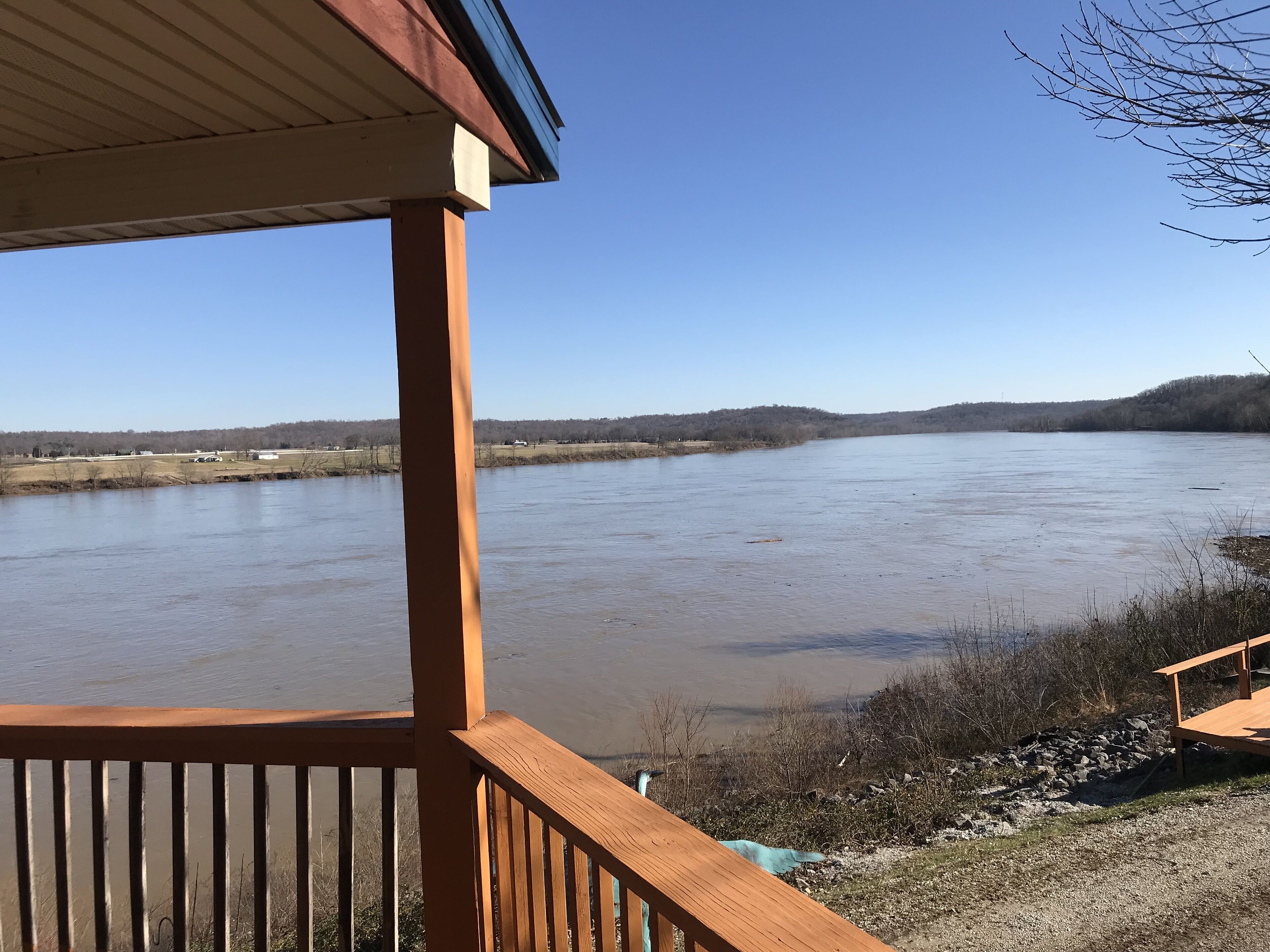 A view from a wooden deck overlooking a river with a distant forested hill.