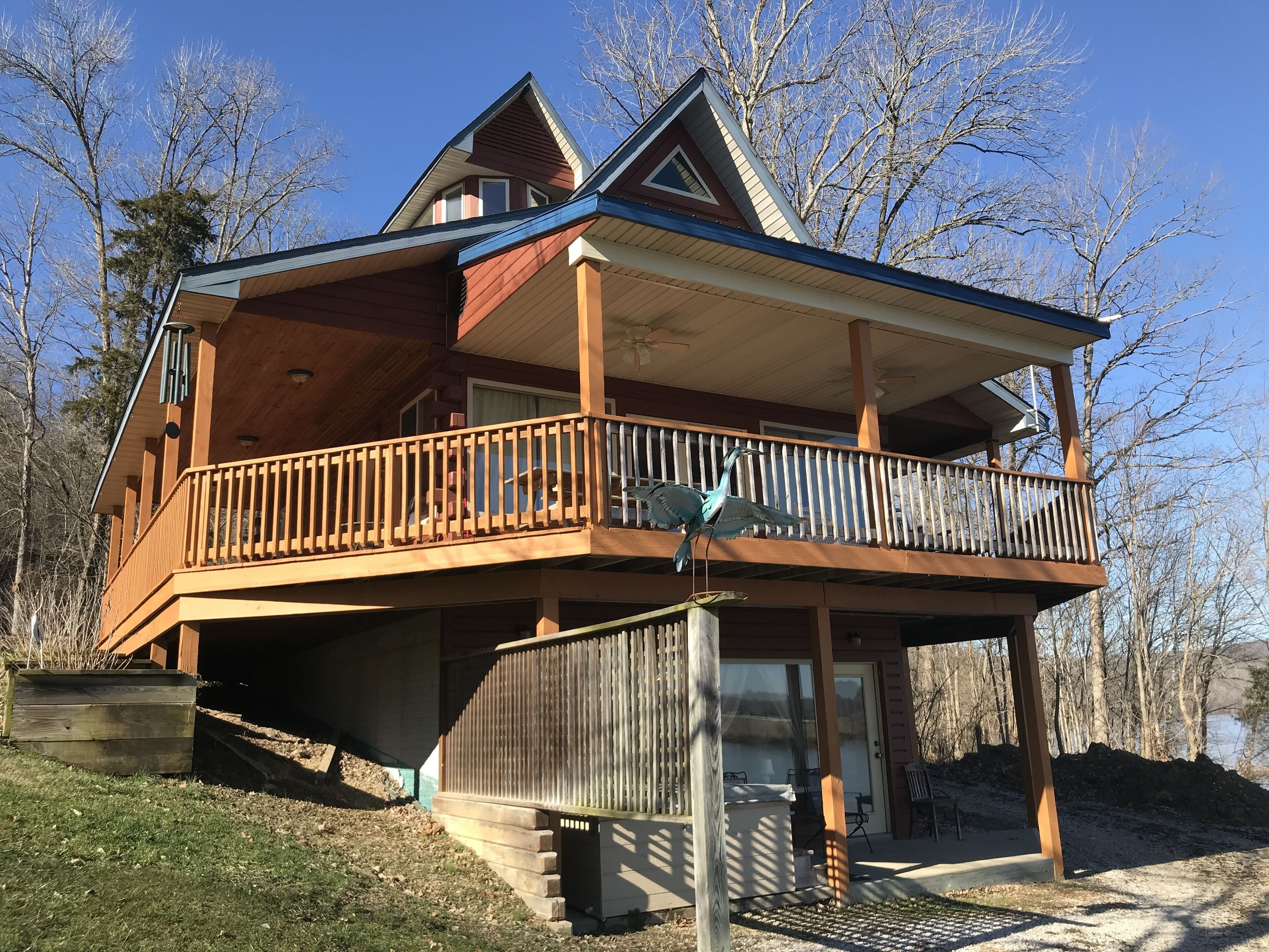 A two-story wooden house with a balcony, a covered porch, and a view of a lake.