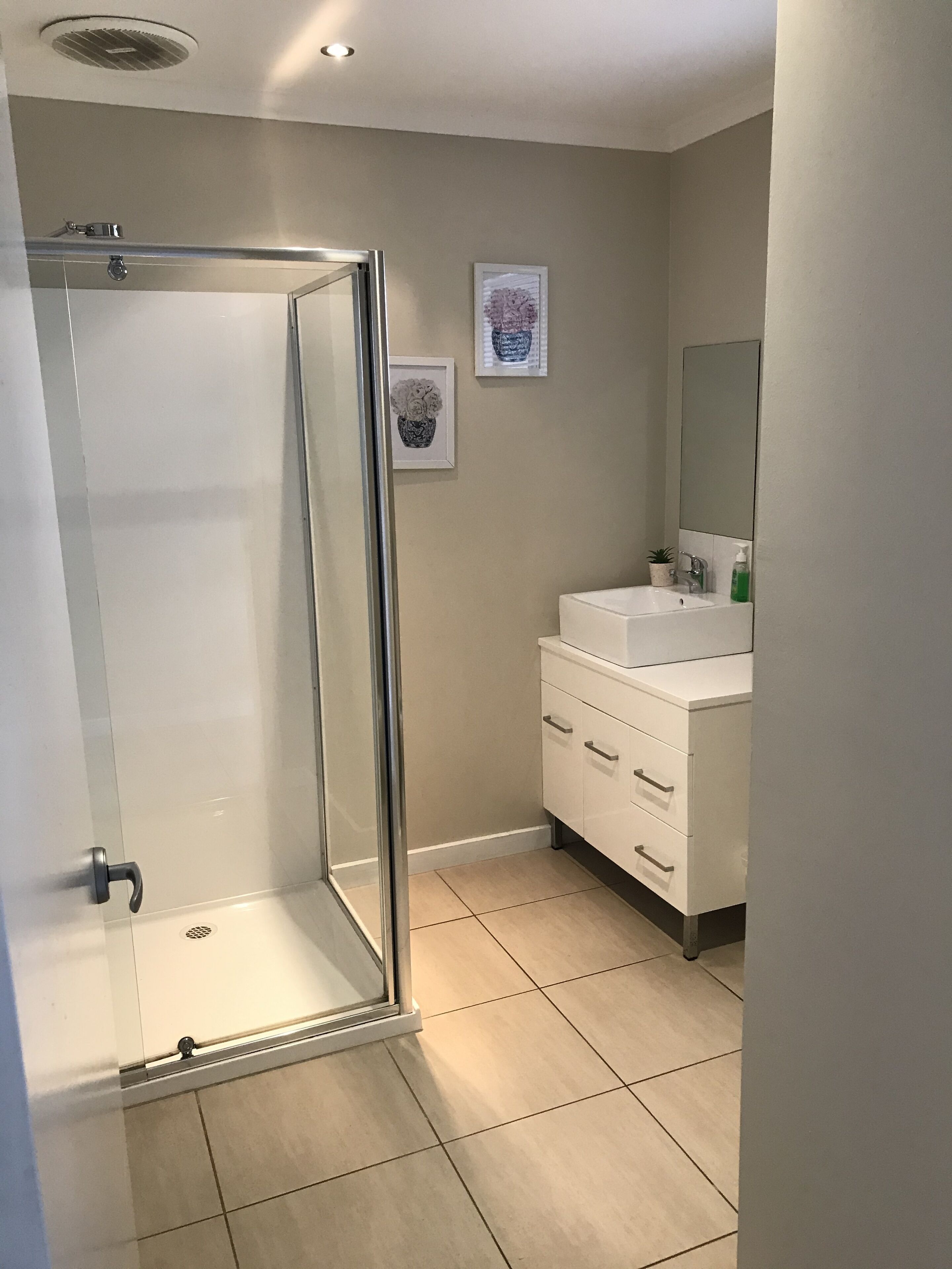 A modern bathroom with a glass shower enclosure, a white vanity with a mirror, and a tiled floor.