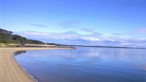Kaarevareunainen ranta, tyyni vesi ja kauempana näkyvä kivikko.