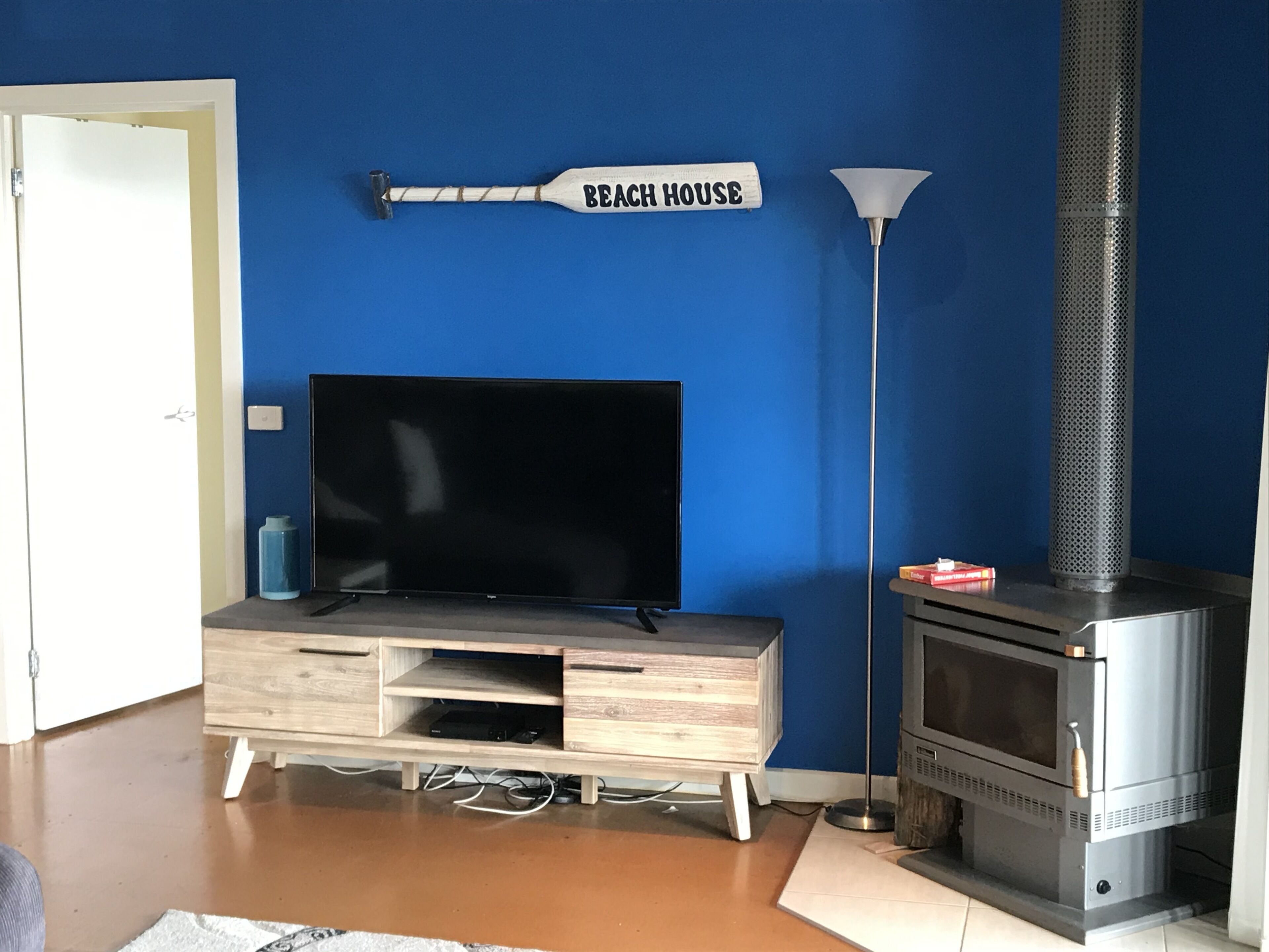 A living room with a flat-screen TV, a wooden entertainment unit, a fireplace, and a lamp.