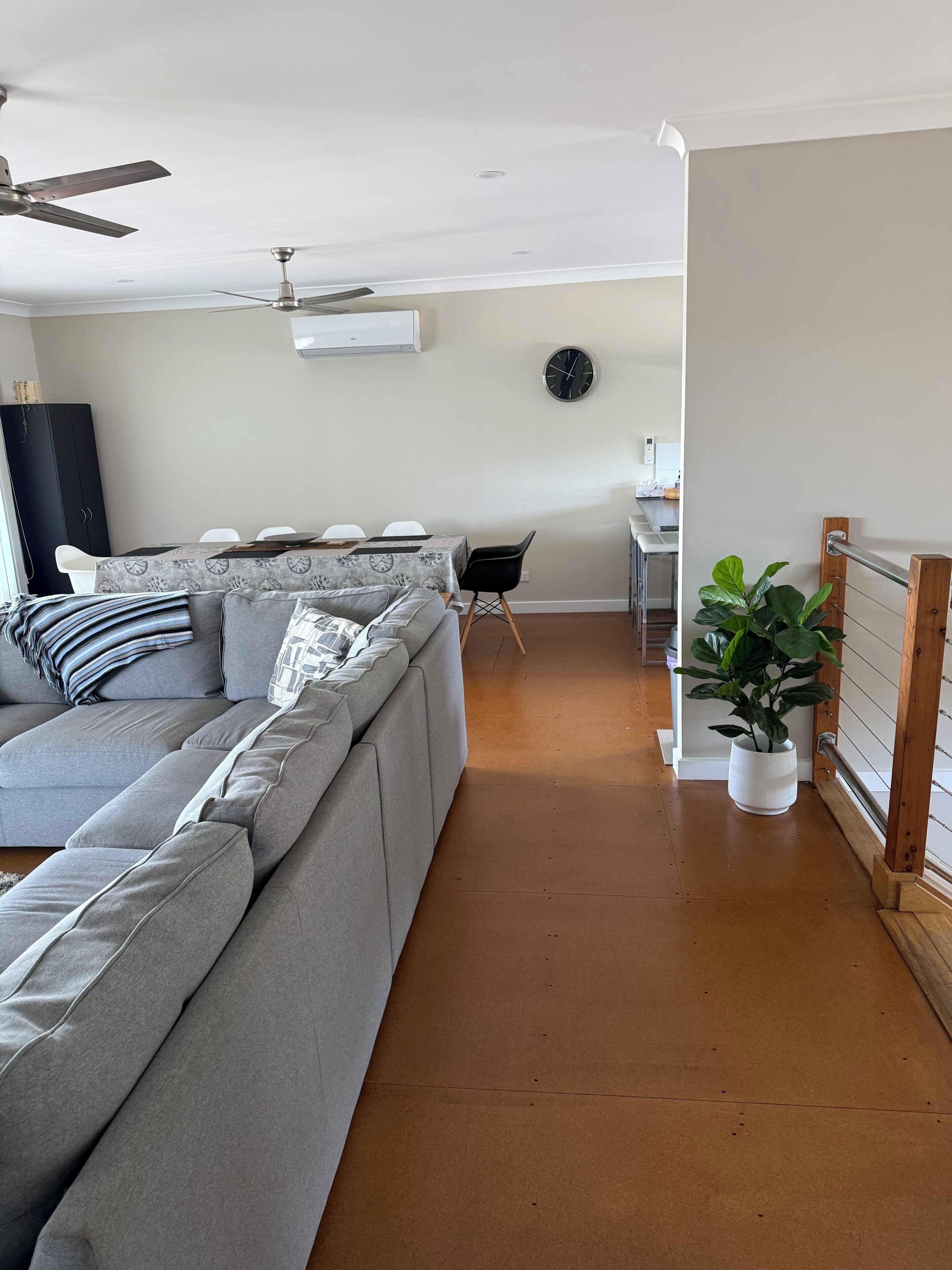 Una sala de estar moderna con un sofá seccional gris, una zona de comedor con una mesa y sillas, una planta en maceta y un ventilador de techo.