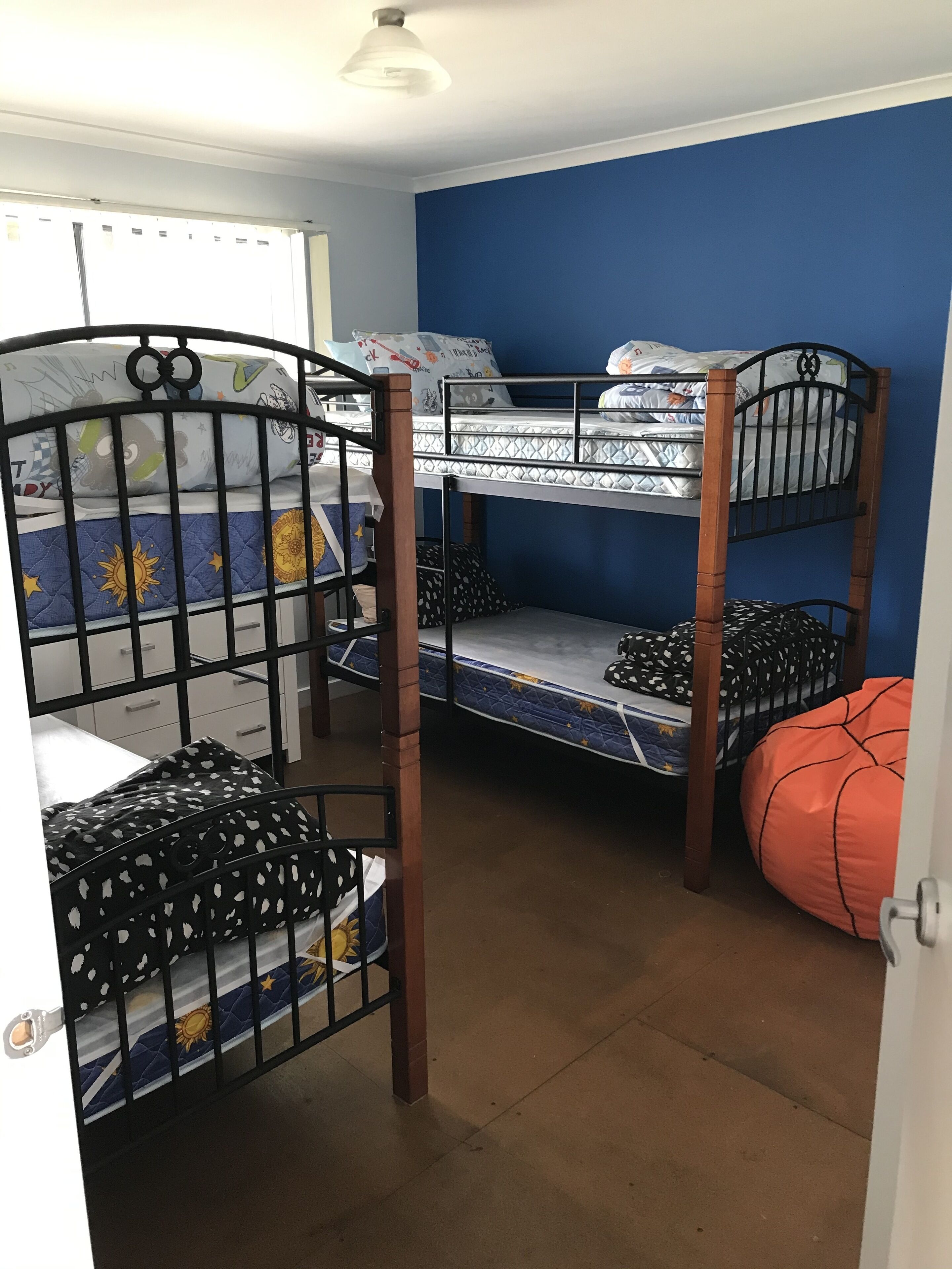 Dormitorio con literas, pared azul, puerta blanca y sillón de pie en forma de balón de baloncesto.