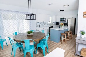 A modern kitchen with white cabinets, a wooden dining table, and turquoise chairs. - Family friendly house • walk to beach • heated pool • sleeps 8 (Naples)