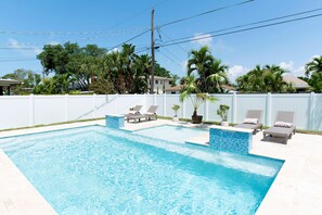 A rectangular swimming pool with a tiled edge, surrounded by a white fence. There are lounge chairs and potted plants along the poolside. - Family friendly house • walk to beach • heated pool • sleeps 8 (Naples)