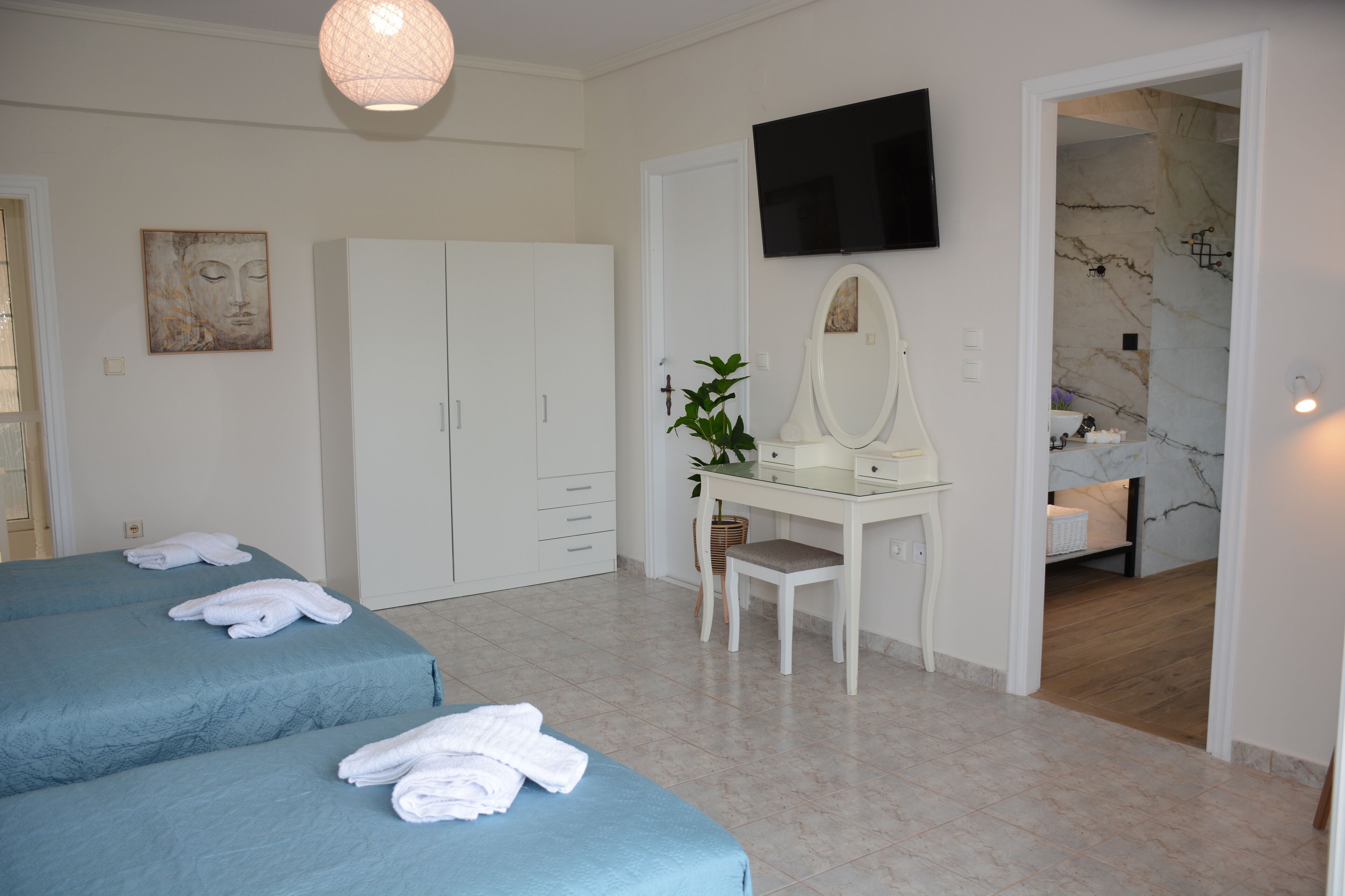 Una camera d'albergo con due letti, una scrivania con uno specchio, una televisione e un bagno parzialmente visibile attraverso una porta aperta.
