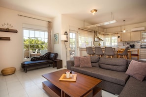 A modern living room with a sofa, coffee table, and a dining area with chairs and a table.