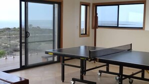 Una mesa de ping pong en una habitación con ventanas amplias y vista al mar.