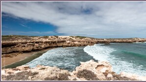Paisaje costero con acantilados rocosos y olas rompiendo contra ellos.