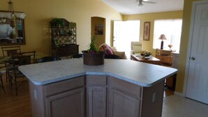 A kitchen with a central island, wooden cabinets, and a dining area with chairs and a table.