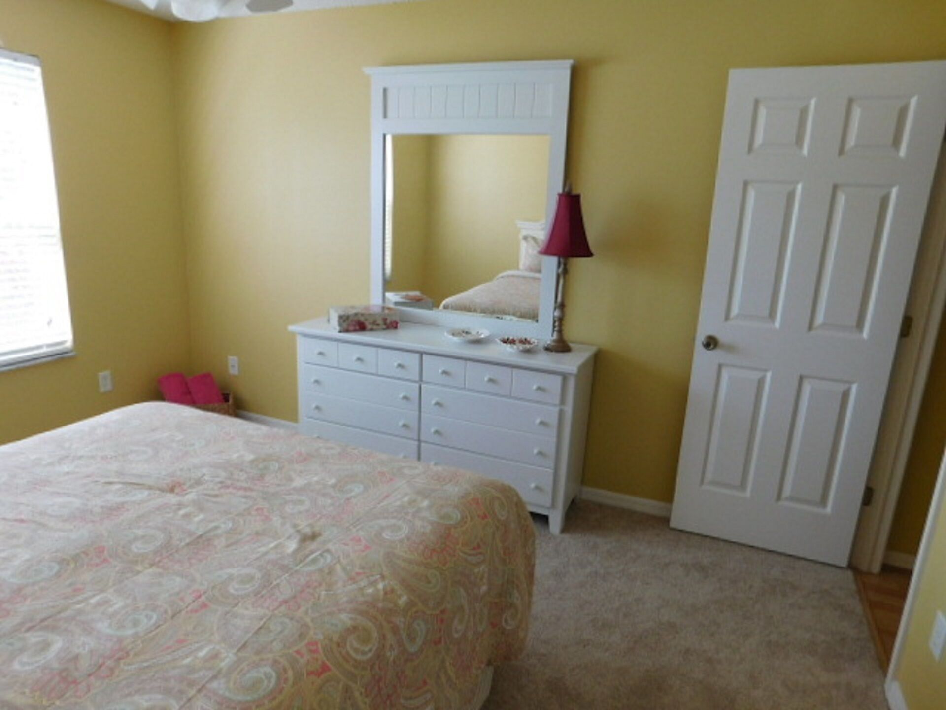 A bedroom with a bed, a dresser, a mirror, and a door.