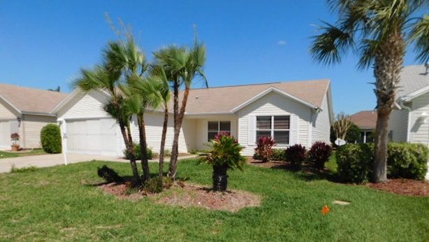 A residential house with a well-maintained lawn, palm trees, and a variety of shrubs.