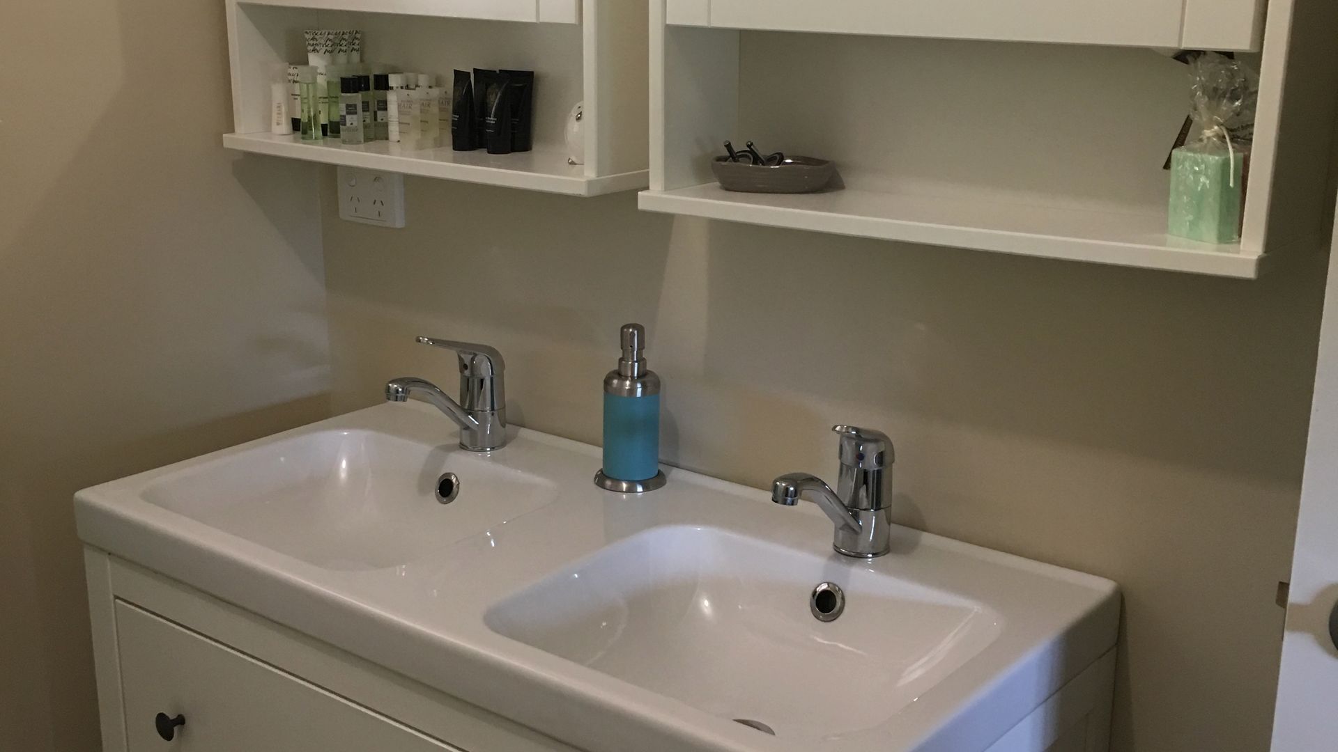 A bathroom with two sinks, a mirror above, and shelves with toiletries.