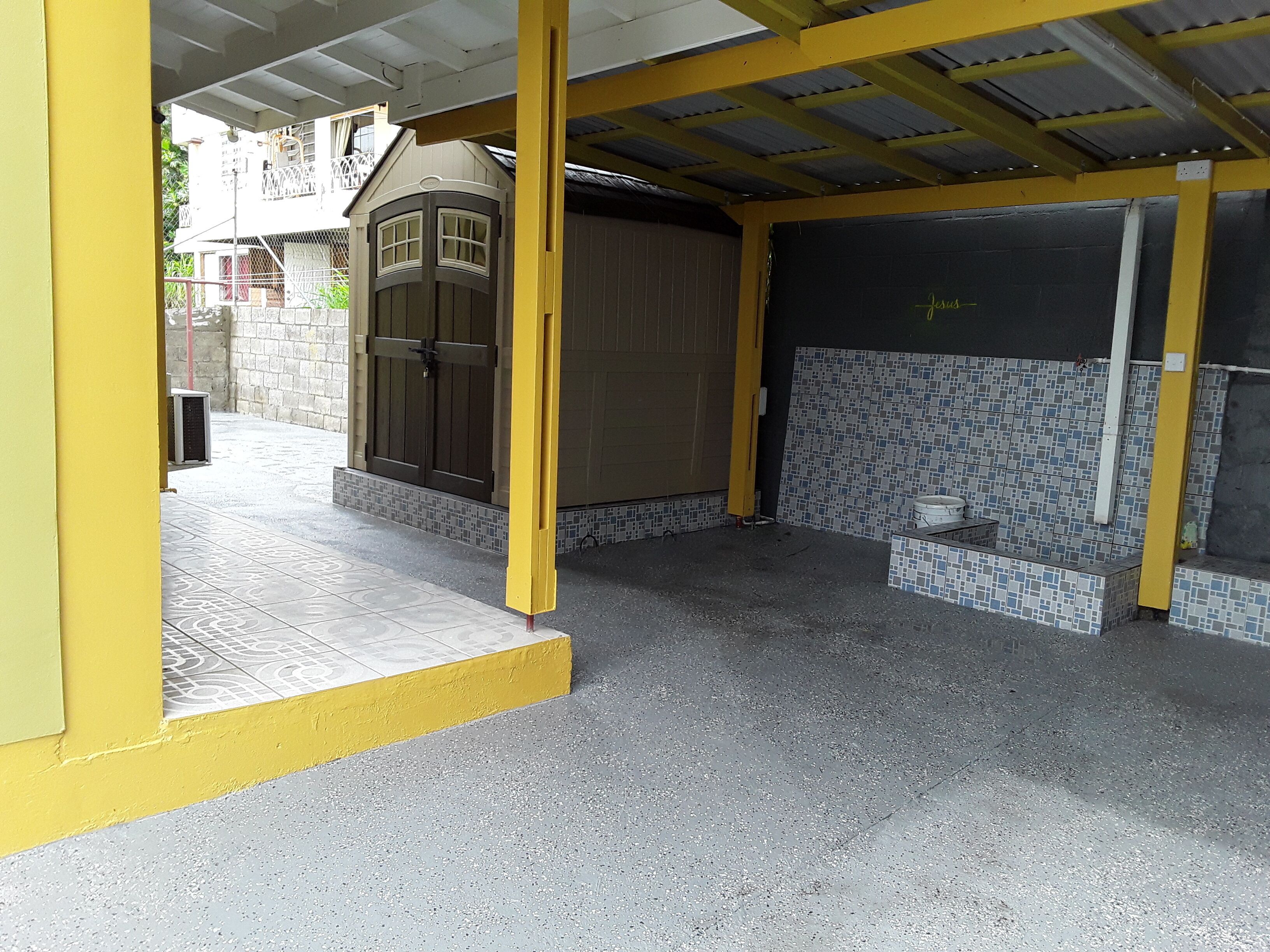 A covered outdoor area with a tiled floor, a brown door, and a tiled wall.
