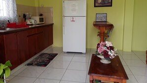 Een keuken met een koelkast, magnetron en spoelbak. Er staat een houten tafel met een bloevas en een fotolijst aan de muur.