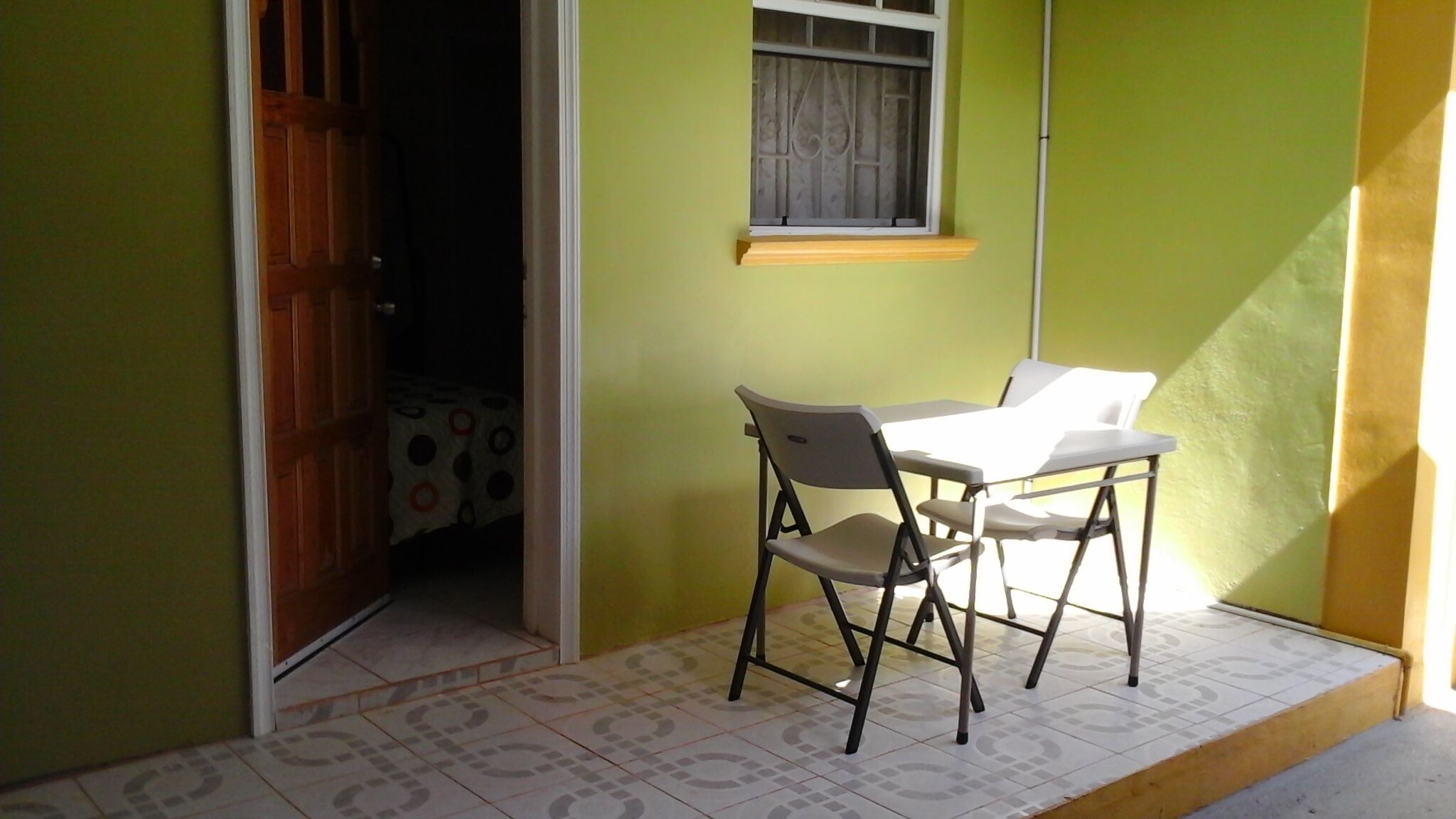 Une petite pièce avec une table et deux chaises, une fenêtre avec un rideau et une porte donnant sur une autre pièce.