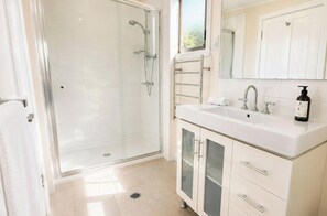 A bathroom with a glass shower enclosure, a white sink with a mirror above, and a towel rack.