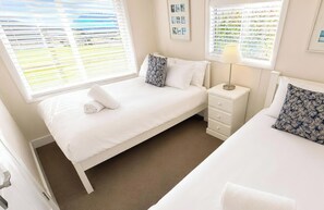 A bedroom with a single bed, a nightstand, a lamp, and a window with blinds.