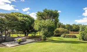 A well-maintained backyard with a wooden deck, a bench, and various trees.