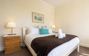 A neatly made bed with a brown blanket, two bedside lamps, a wooden nightstand with drawers, and a framed picture on the wall.