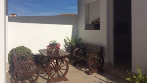Un patio con una mesa y un banco de madera, una planta en maceta y una ventana con flores.
