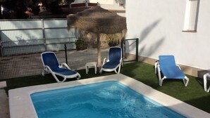 Una piscina con agua azul, rodeada de sillas blancas junto a la piscina y una pequeña mesa blanca.