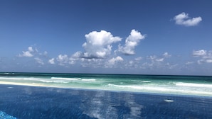 Helderblauwe lucht met wolken, een zandstrand en een zwembad.