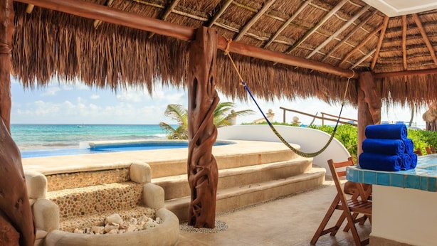 Een strandlounge met rieten dak, een zwembad en een zitgedeelte met uitzicht op de oceaan.
