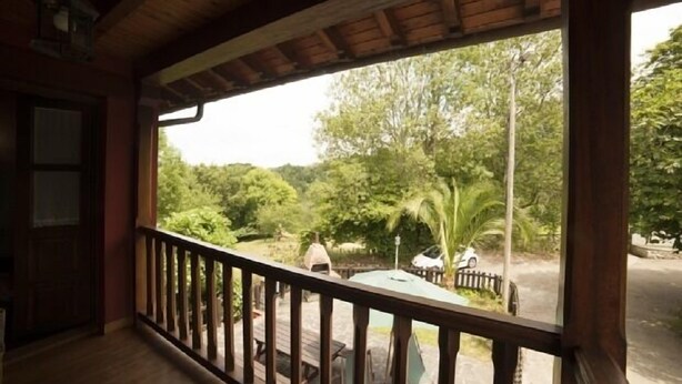 A wooden balcony with a view of a lush garden and a parked car. - Rural house El Campón de San Martín II for 4 people (Piloña)