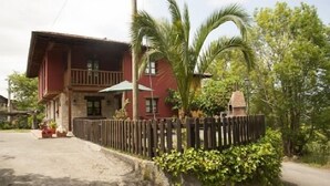A two-story house with a balcony, surrounded by a wooden fence and lush greenery. - Rural house El Campón de San Martín II for 4 people (Piloña)