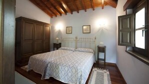 A bedroom with a wooden ceiling, a bed with patterned bedding, two bedside tables, and a window with a view. - Rural house El Campón de San Martín II for 4 people (Piloña)