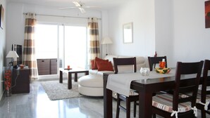 A modern living room with a dining area, a sofa, a coffee table, and a ceiling fan. - Cozy apartment with beautiful view on golf course, mountains and nature reserve. (Alhaurin El Grande)