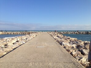A concrete pathway leading to a rocky shoreline with calm water. - Cozy apartment with beautiful view on golf course, mountains and nature reserve. (Alhaurin El Grande)