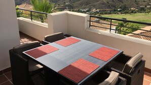 A balcony with a table and chairs, overlooking a hilly landscape with houses and greenery. - Cozy apartment with beautiful view on golf course, mountains and nature reserve. (Alhaurin El Grande)