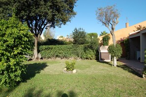 Um jardim bem cuidado com gramado, arbusto pequeno e diversas árvores.