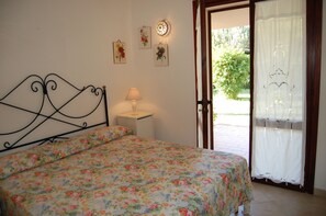 Quarto com colcha florida, abajur e luminária na parede.