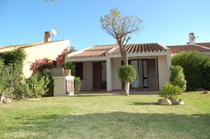 Uma casa de dois andares com telhado de telhas, um pequeno jardim com uma árvore e uma antena parabólica.