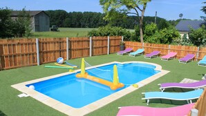 A backyard with a swimming pool, artificial grass, and several lounge chairs.