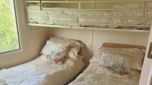 A room with two beds, each with a headboard and pillows, and a window providing a view of greenery.