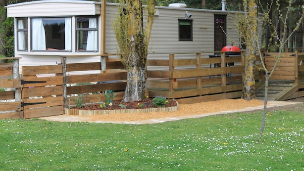 A mobile home with a fenced yard, a small garden, and a wooden deck.