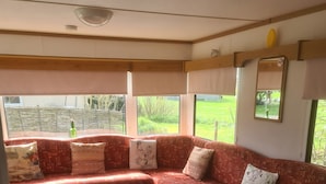 A cozy interior with a red patterned sofa, a table with a strawberry pattern, and a view of a green landscape through large windows.