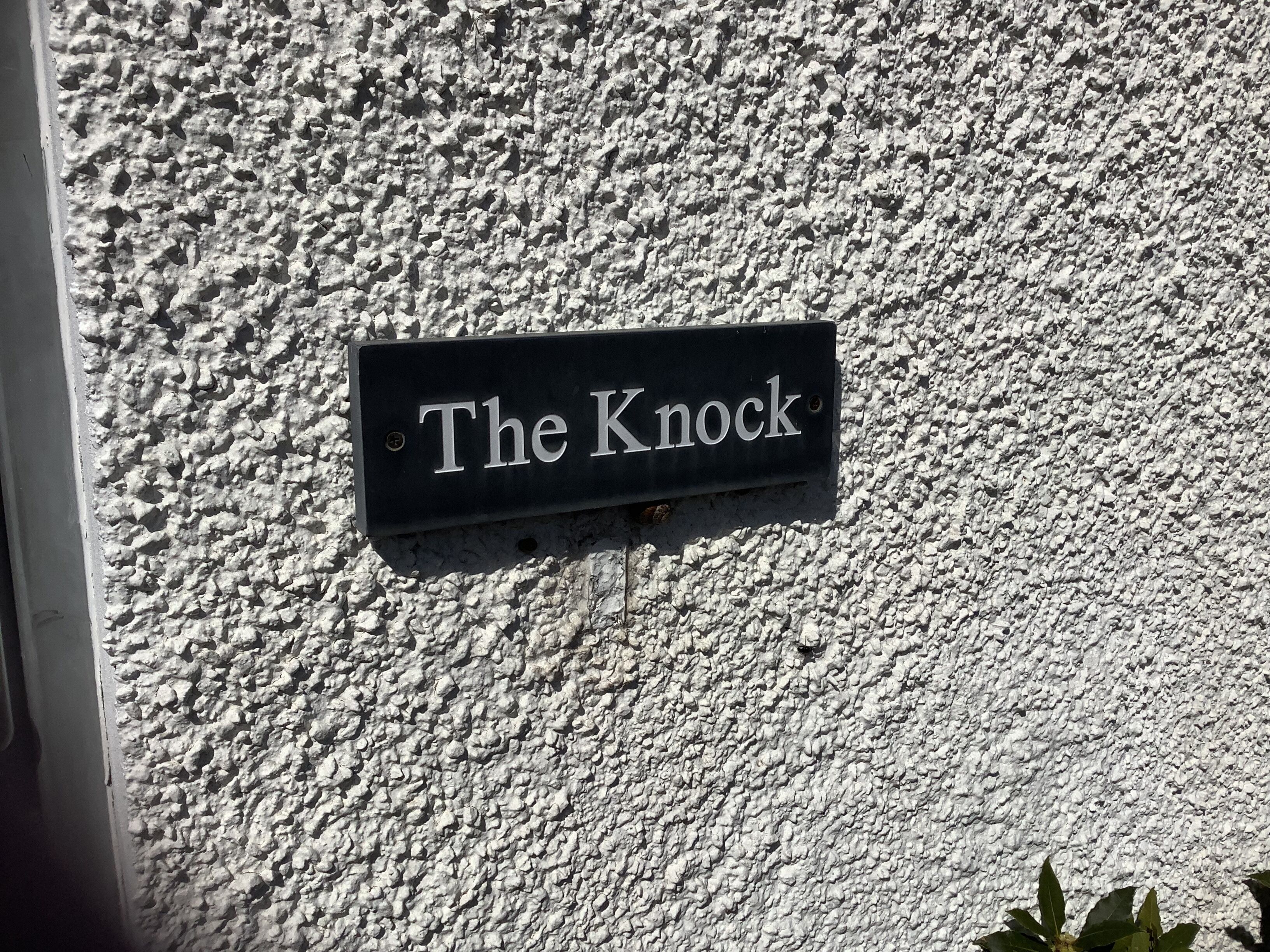 Un letrero negro con letras blancas sobre una pared texturizada, que dice 'The Knock'.